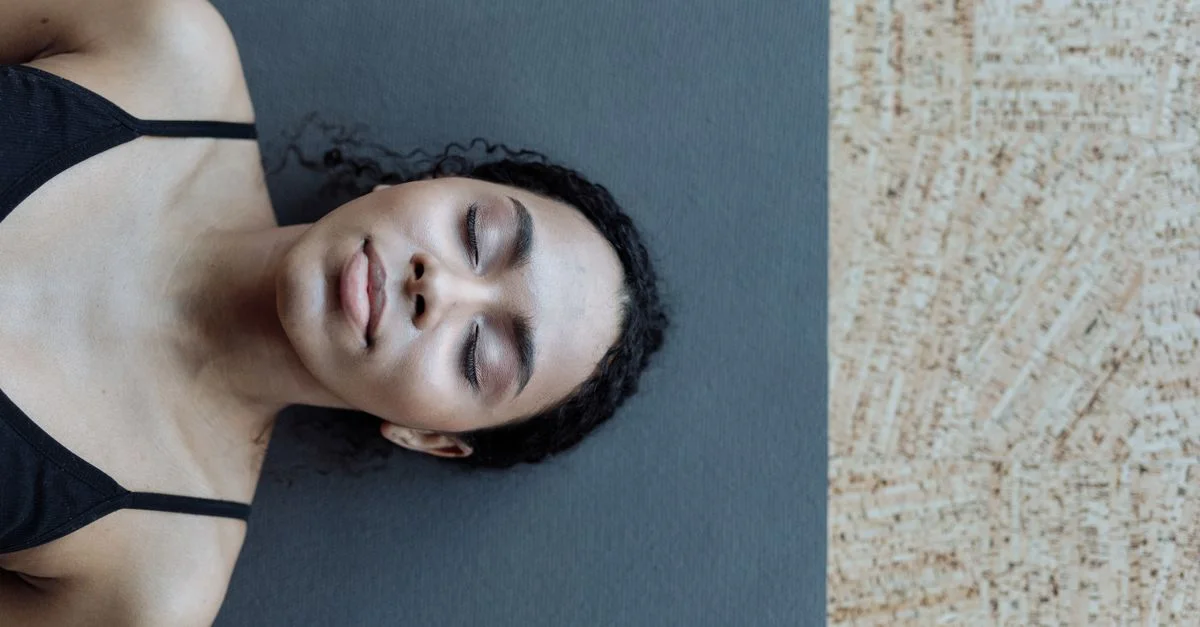 Un portrait serein d'une femme aux cheveux bouclés allongée sur un tapis de yoga à l'intérieur, dégageant une sensation de calme.