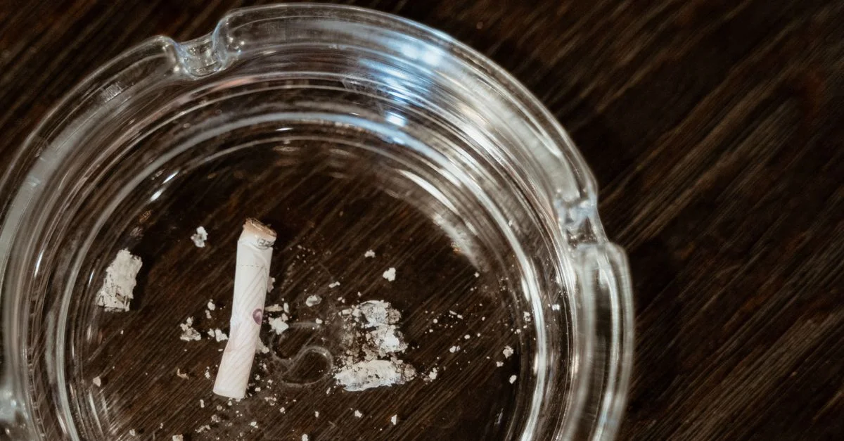 Un gros plan d'un mégot de cigarette dans un cendrier en verre sur une table en bois.
