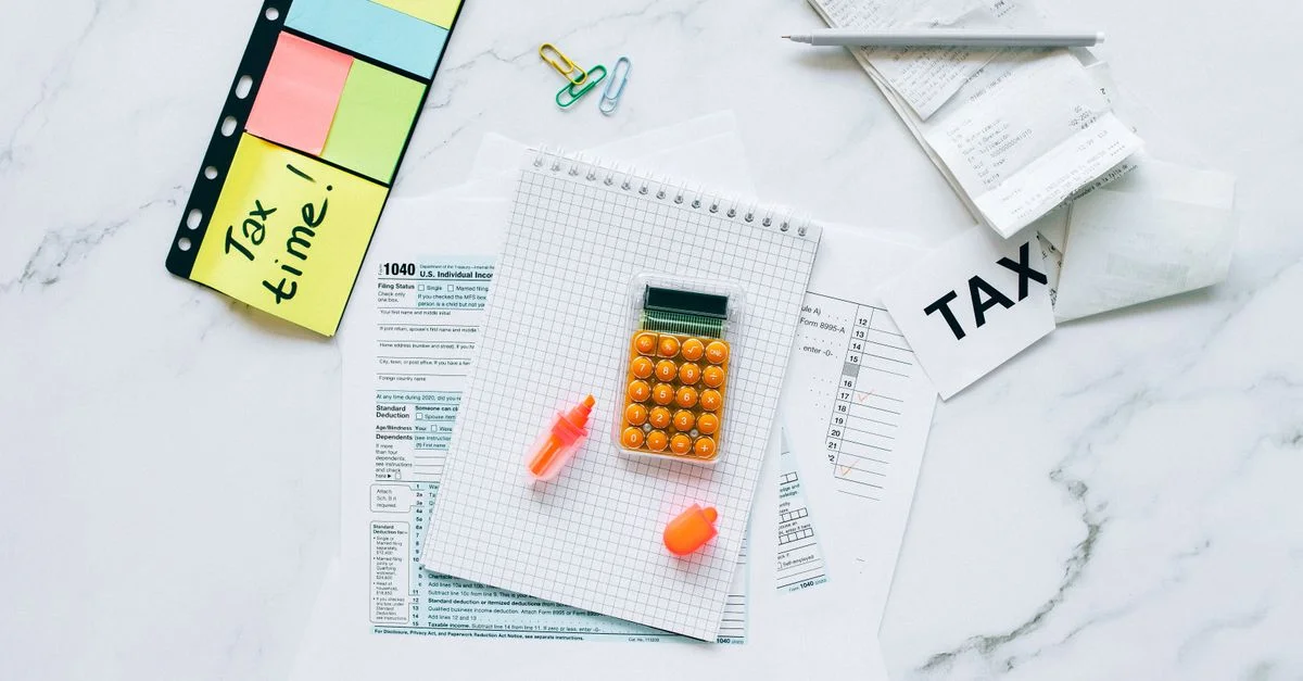 Vue de dessus des essentiels pour la préparation des impôts avec calculatrice, formulaires et notes autocollantes colorées.