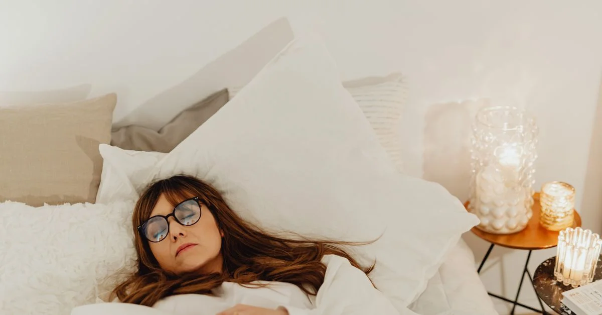 Une femme se reposant paisiblement dans son lit avec un éclairage tamisé et une literie blanche douce.