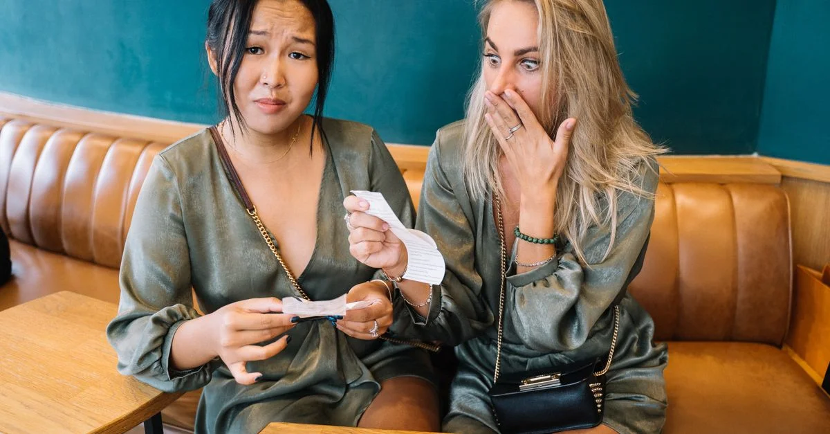 Deux femmes expriment leur surprise en examinant une facture de restaurant dans un cadre décontracté.