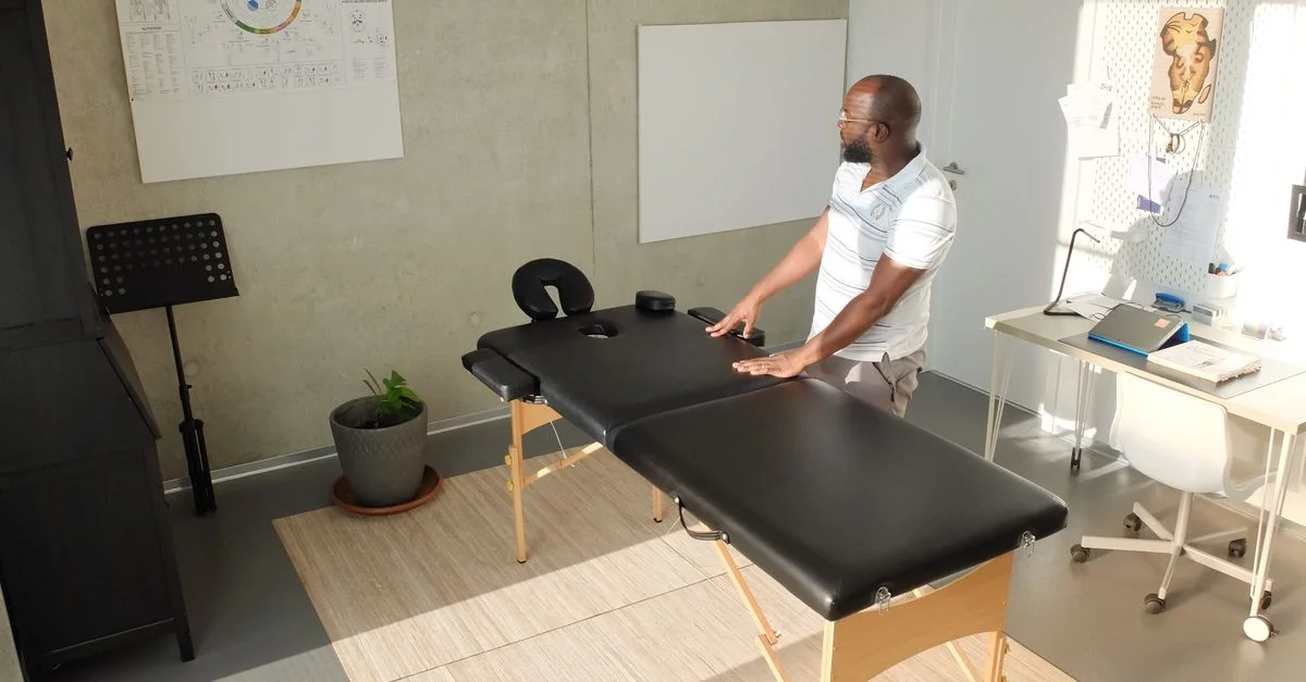 Un physiothérapeute se tenant à côté d'une table de massage dans un bureau de santé moderne et lumineux.