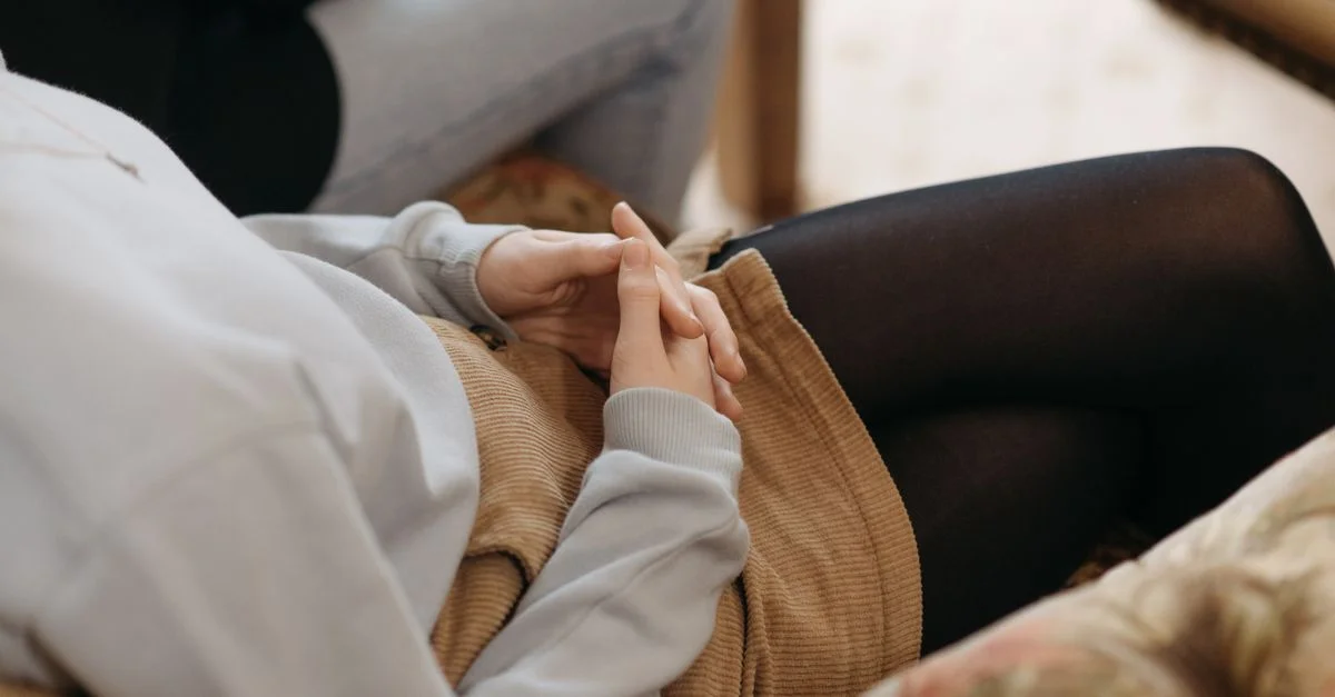 Gros plan sur les mains d'un adolescent jointes lors d'une séance de conseil, symbolisant la contemplation.