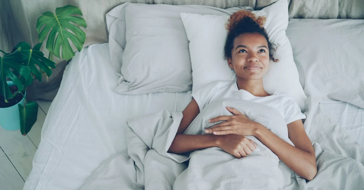 Femme se détendant au lit avec une plante monstera, profitant d'une matinée tranquille.